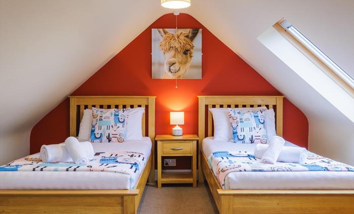 Large alpaca wall canvas above two full size single beds with side table and lamp and alpaca and Peruvian design accessories.